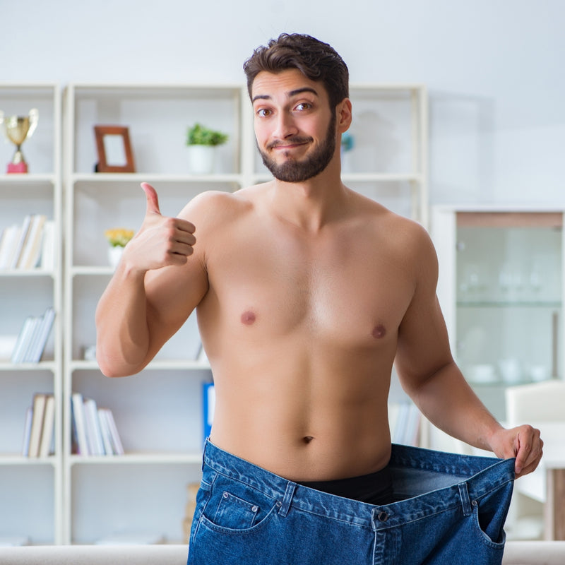 Man showing off weight loss by wearing a large pair of jeans indoors.